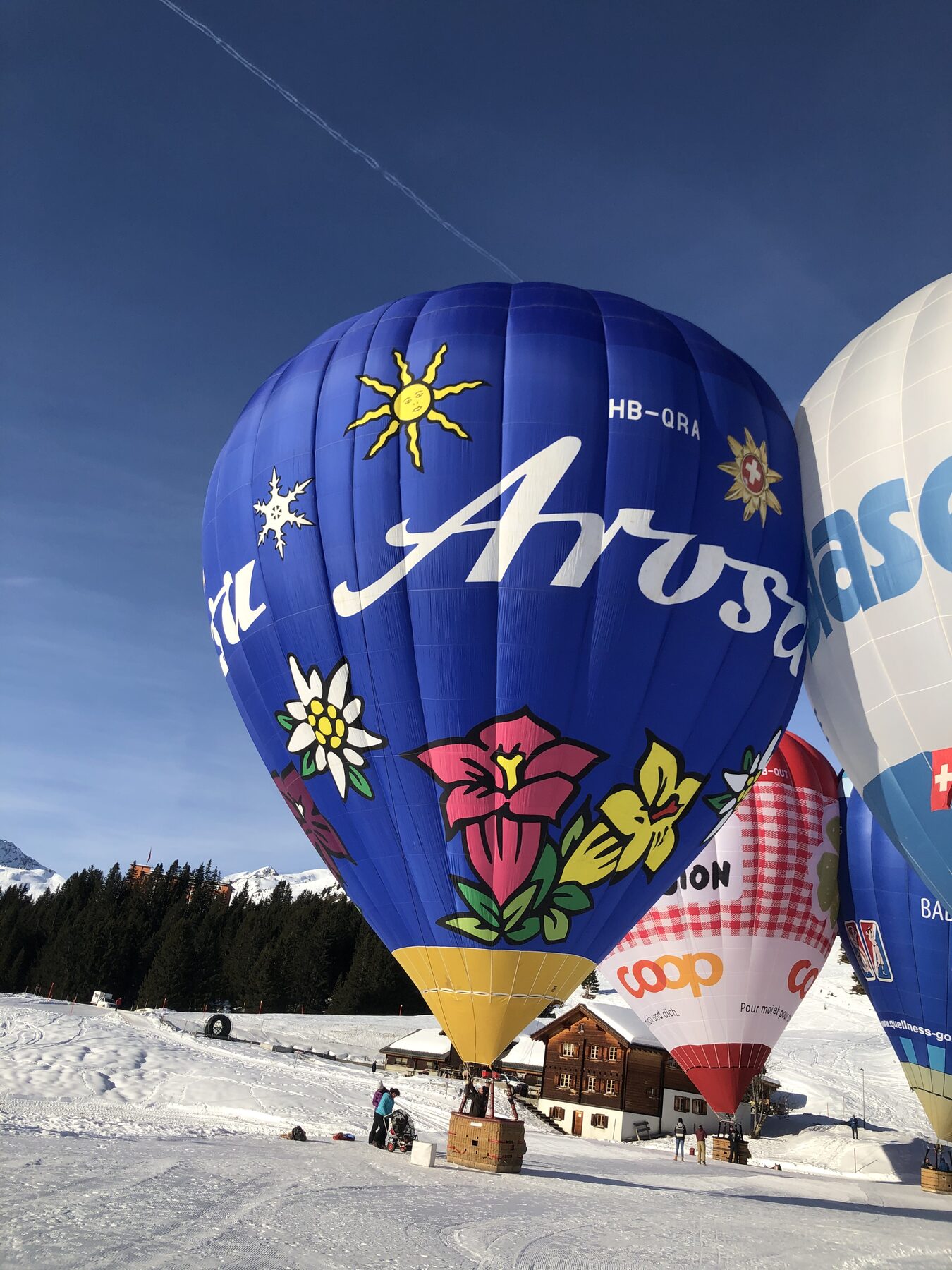 Heißluftballone auf dem verschneiten Feld, davor ein Chalet