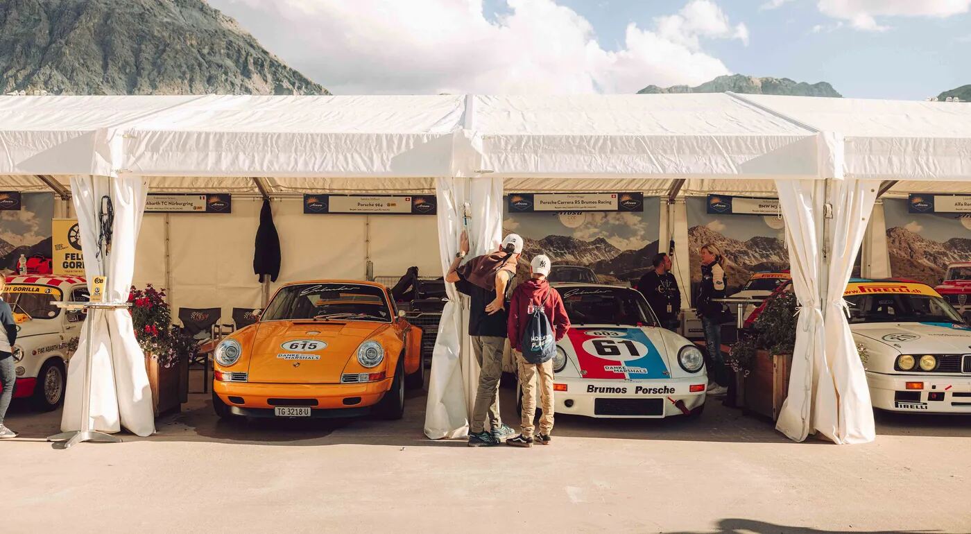 Klassische Rennwagen unter den Zeltdächern des Fahrerlagers, dahinter die Berge