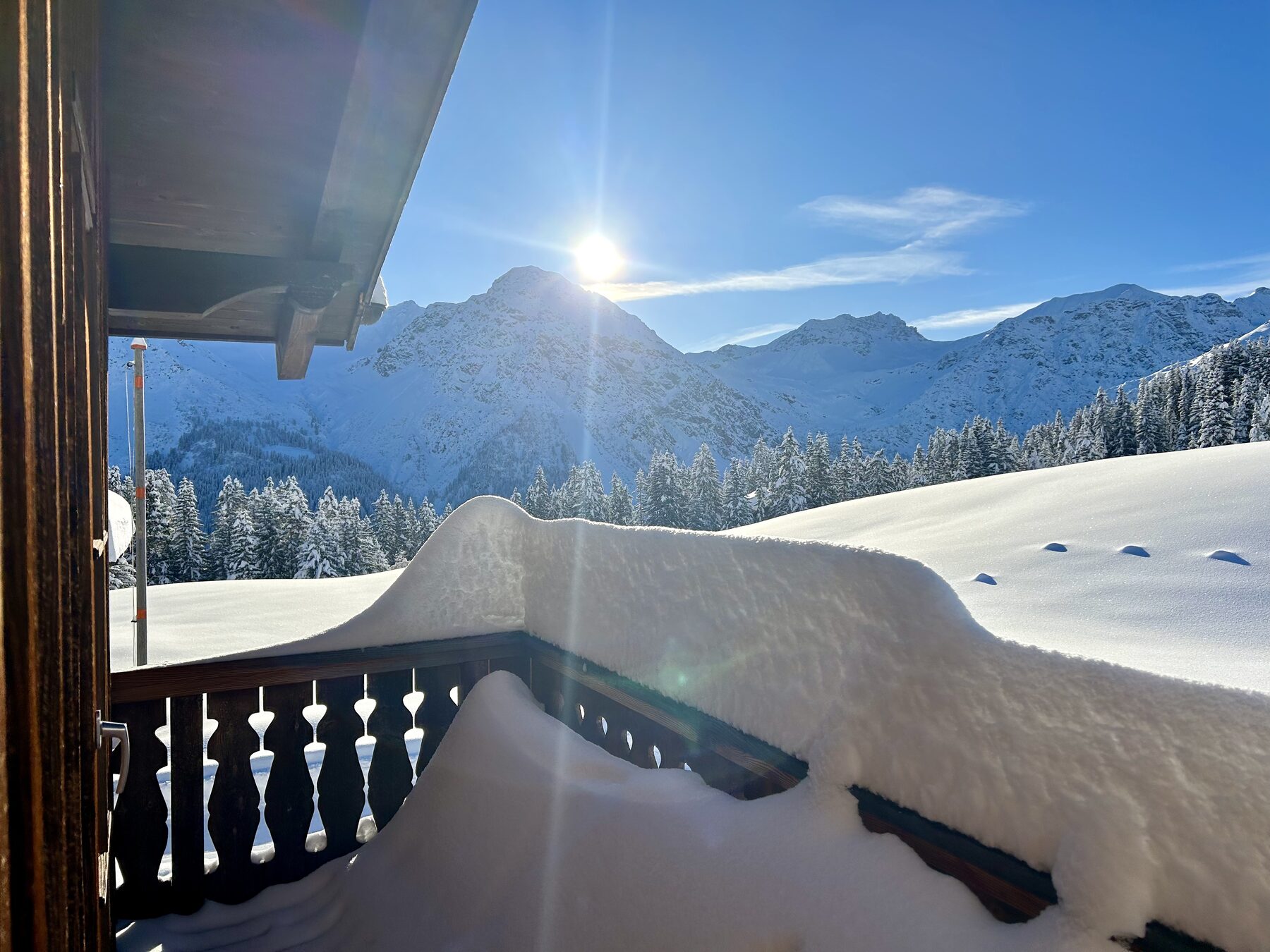 Derselbe Balkon unter der Schneelast, dahinter die Sonne über den Bergen