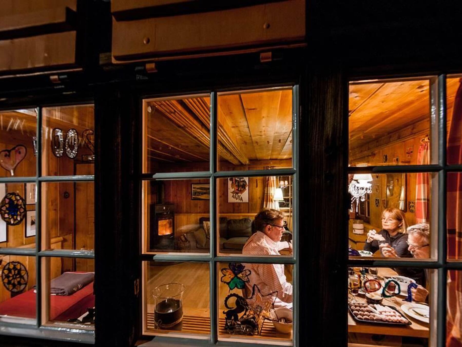 Blick durch das Fenster in die erleuchtete Stube, abends am Tisch